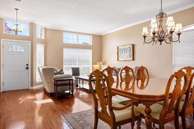 dining space with wood-type flooring, ornamental molding, a notable chandelier, and a textured ceiling