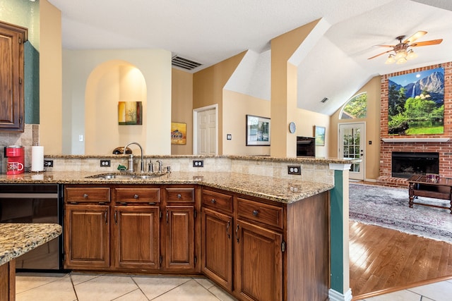 kitchen featuring a brick fireplace, sink, kitchen peninsula, black dishwasher, and light hardwood / wood-style flooring