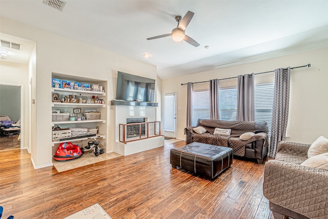 living room with wood-type flooring, built in shelves, and ceiling fan