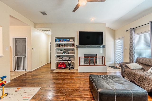 living room featuring ceiling fan, hardwood / wood-style flooring, vaulted ceiling, and built in shelves