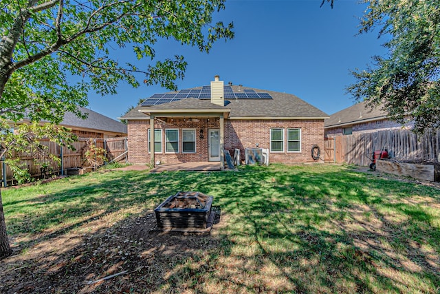 back of property featuring solar panels, a yard, and an outdoor fire pit