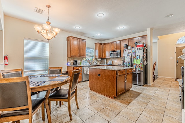 kitchen with pendant lighting, a kitchen island, a notable chandelier, stainless steel appliances, and backsplash