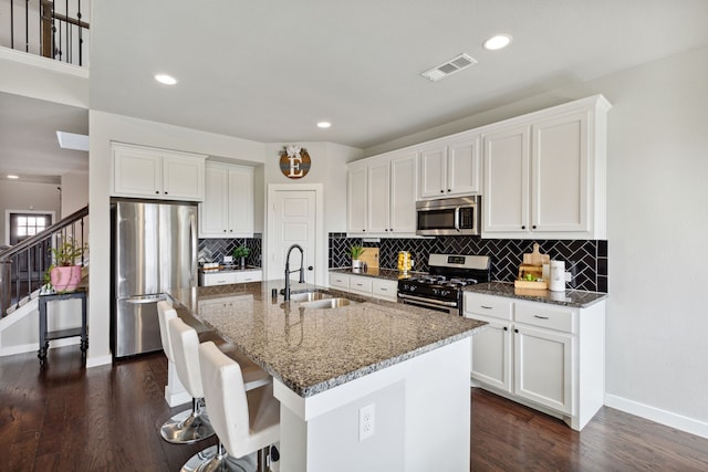 kitchen featuring a kitchen island with sink, stainless steel appliances, dark wood-type flooring, sink, and white cabinetry