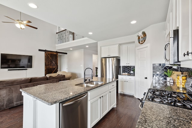 kitchen featuring a barn door, a center island with sink, sink, appliances with stainless steel finishes, and white cabinetry