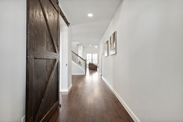 corridor with a barn door and dark hardwood / wood-style flooring