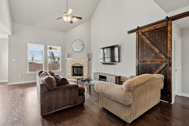 living room featuring ceiling fan, dark wood-type flooring, high vaulted ceiling, a fireplace, and a barn door