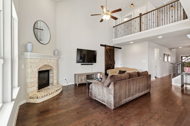 living room featuring ceiling fan, dark hardwood / wood-style floors, a fireplace, a barn door, and a towering ceiling