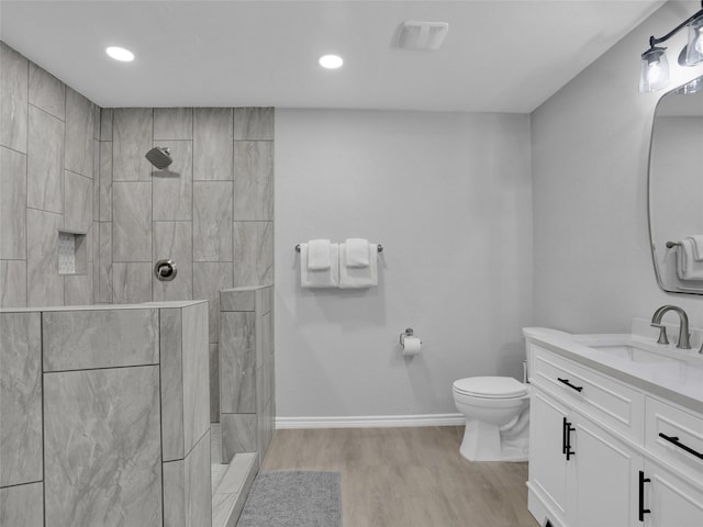 bathroom featuring vanity, hardwood / wood-style floors, a tile shower, and toilet