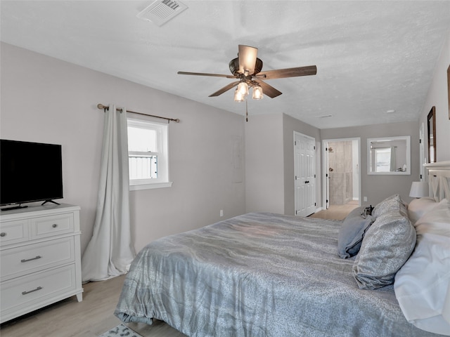 bedroom featuring connected bathroom, light hardwood / wood-style flooring, a textured ceiling, and ceiling fan