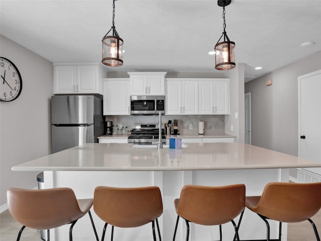 kitchen with a large island with sink, decorative backsplash, stainless steel appliances, hanging light fixtures, and white cabinetry