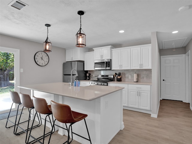 kitchen featuring a kitchen island with sink, light wood-type flooring, a kitchen breakfast bar, white cabinets, and appliances with stainless steel finishes