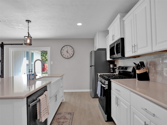 kitchen with a barn door, white cabinetry, light hardwood / wood-style flooring, appliances with stainless steel finishes, and decorative light fixtures