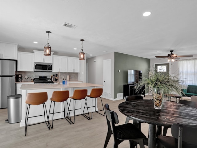 kitchen featuring white cabinets, hanging light fixtures, a large island with sink, light hardwood / wood-style flooring, and stainless steel appliances