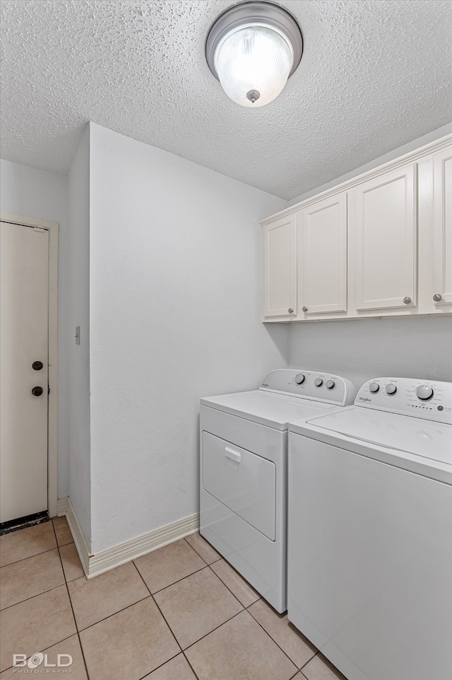 washroom with washing machine and clothes dryer, cabinets, light tile patterned floors, and a textured ceiling