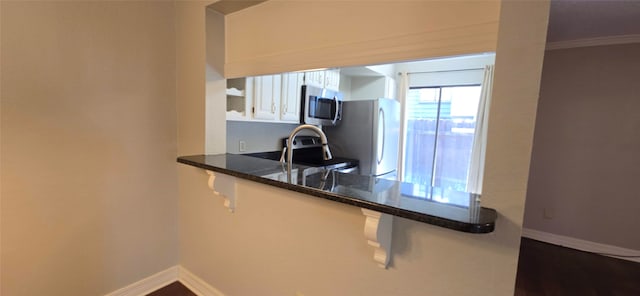 kitchen featuring dark stone countertops, crown molding, stainless steel appliances, and white cabinets