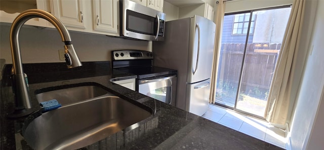 kitchen featuring stainless steel appliances, tile patterned flooring, sink, and dark stone counters