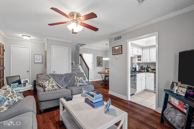 living room with ceiling fan with notable chandelier, a textured ceiling, ornamental molding, and light hardwood / wood-style flooring