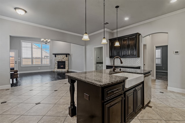 kitchen featuring light stone counters, an island with sink, stainless steel dishwasher, and ornamental molding