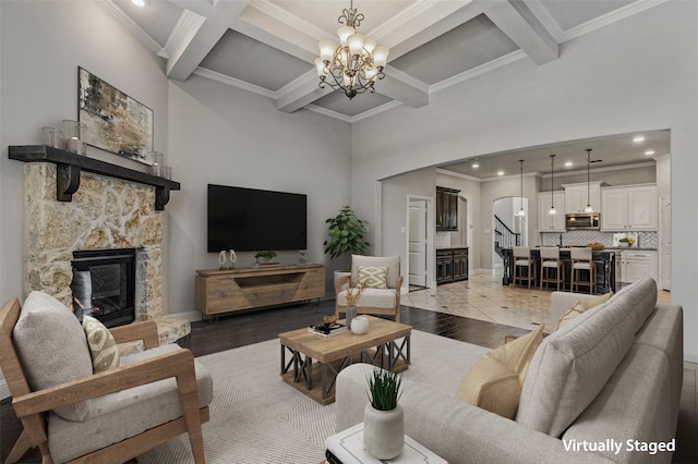 living room with coffered ceiling, an inviting chandelier, light hardwood / wood-style flooring, a fireplace, and ornamental molding