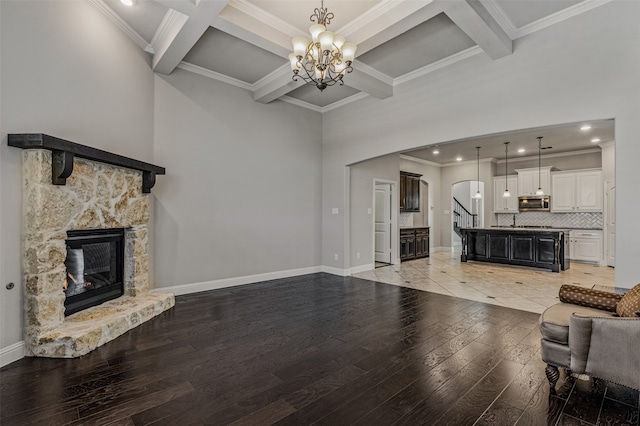 living room with coffered ceiling, an inviting chandelier, a stone fireplace, light hardwood / wood-style flooring, and crown molding