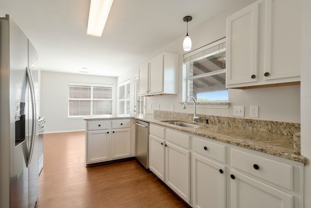 kitchen with stainless steel appliances, hardwood / wood-style flooring, sink, pendant lighting, and white cabinetry