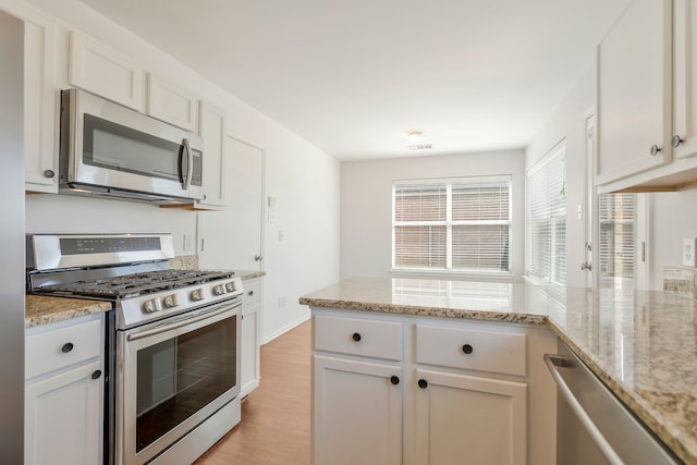 kitchen with light stone counters, white cabinetry, stainless steel appliances, and light hardwood / wood-style flooring