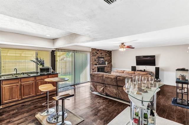 living room featuring a brick fireplace, a textured ceiling, and dark wood-type flooring