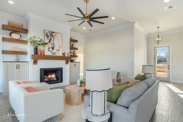 living room featuring ceiling fan with notable chandelier, a large fireplace, and crown molding