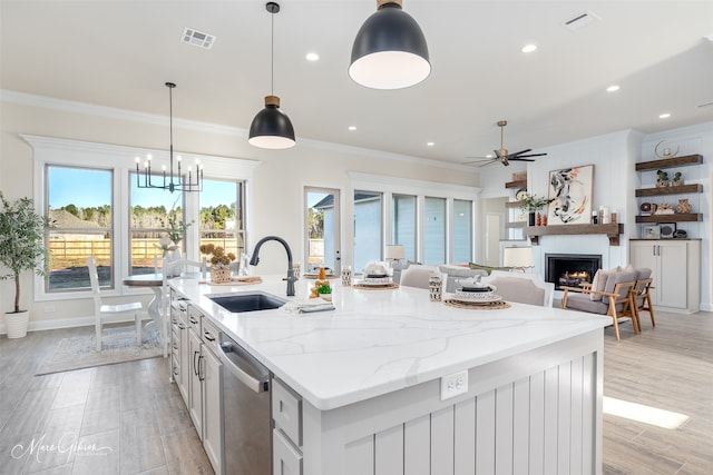 kitchen featuring light stone countertops, stainless steel dishwasher, a kitchen island with sink, sink, and hanging light fixtures