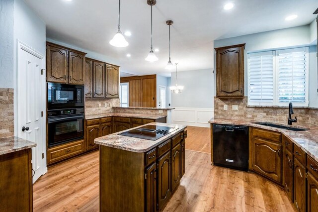 kitchen featuring hanging light fixtures, a center island, light stone counters, and black appliances