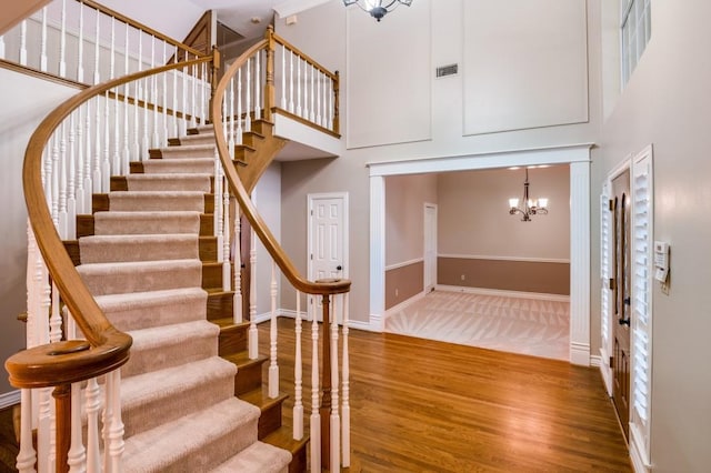 stairs featuring an inviting chandelier, a towering ceiling, and hardwood / wood-style flooring