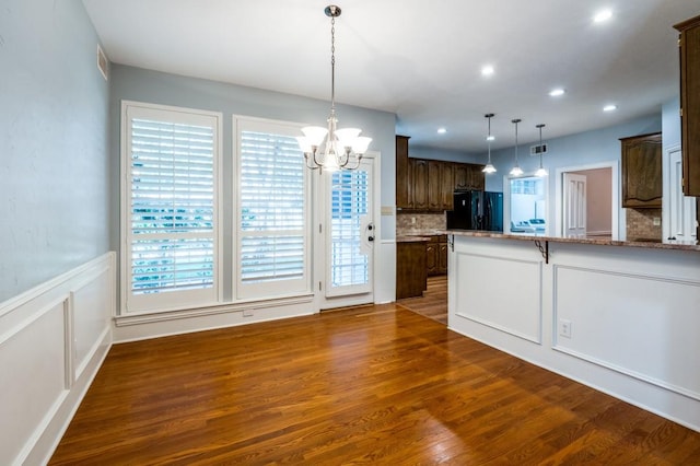 kitchen featuring pendant lighting, dark hardwood / wood-style floors, black fridge, and a healthy amount of sunlight