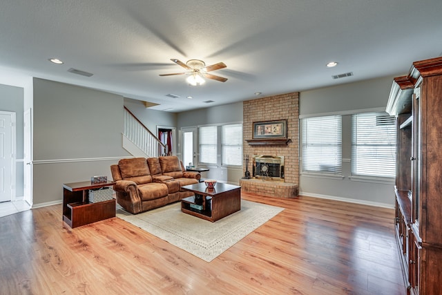 living room featuring ceiling fan, wood-type flooring, a textured ceiling, and a brick fireplace