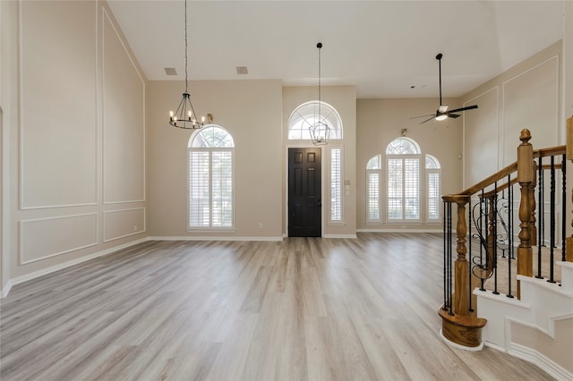 foyer entrance featuring ceiling fan with notable chandelier, light wood-type flooring, and a towering ceiling