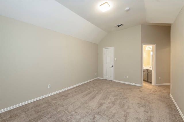 unfurnished bedroom with lofted ceiling, ensuite bath, and light carpet