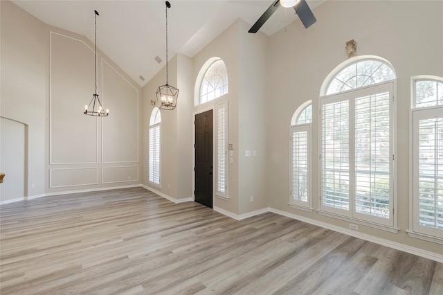 foyer entrance featuring ceiling fan with notable chandelier, light hardwood / wood-style floors, and high vaulted ceiling