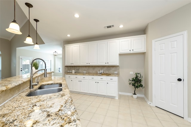 kitchen with light stone countertops, white cabinets, decorative light fixtures, and sink