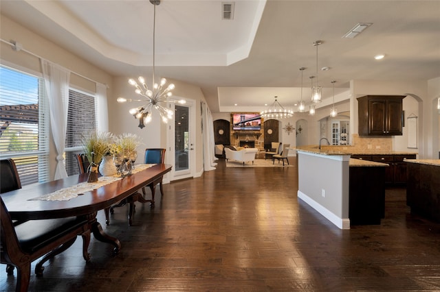 dining area with a raised ceiling, a chandelier, dark hardwood / wood-style flooring, and sink