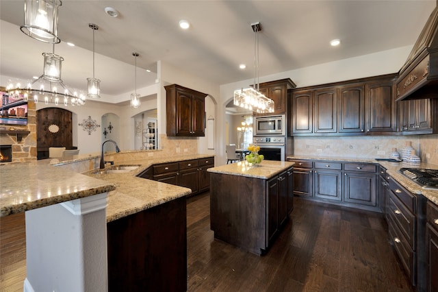 kitchen featuring dark brown cabinetry, dark hardwood / wood-style flooring, pendant lighting, kitchen peninsula, and appliances with stainless steel finishes