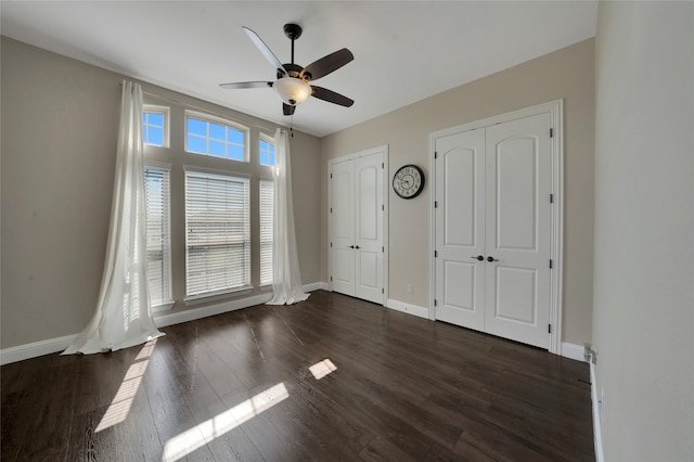 unfurnished bedroom featuring two closets, dark hardwood / wood-style floors, and ceiling fan