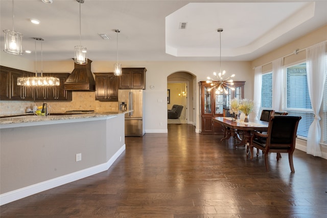 kitchen with high end fridge, dark brown cabinetry, dark hardwood / wood-style flooring, and custom exhaust hood