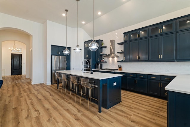 kitchen featuring arched walkways, light countertops, glass insert cabinets, freestanding refrigerator, and wall chimney range hood