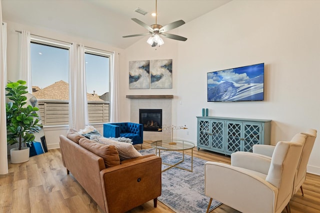 living room with a ceiling fan, wood finished floors, visible vents, a tile fireplace, and vaulted ceiling