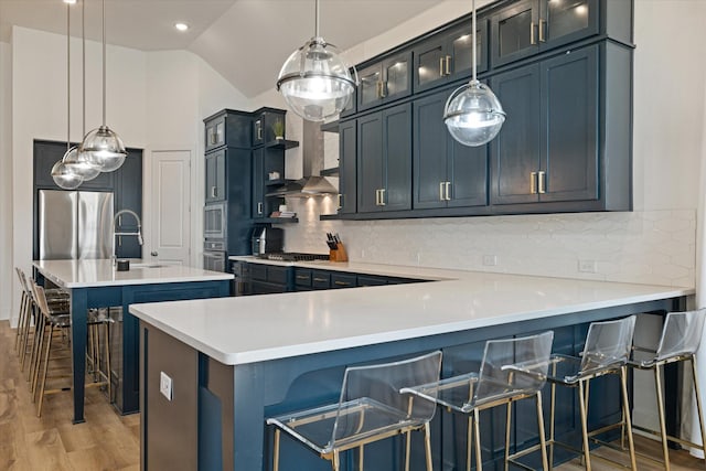 kitchen featuring hanging light fixtures, wall chimney exhaust hood, a kitchen bar, and a sink