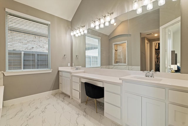 bathroom featuring marble finish floor, a sink, double vanity, baseboards, and vaulted ceiling