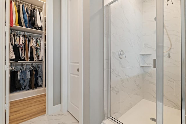 full bathroom featuring marble finish floor, a stall shower, a walk in closet, and baseboards