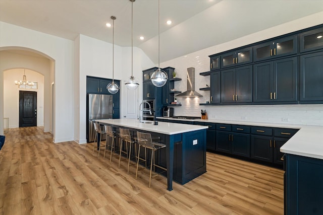 417 Sunnyridge Ln, Little Elm, TX 76227 - kitchen featuring freestanding refrigerator, wall chimney range hood, arched walkways, a breakfast bar area, and light wood finished floors