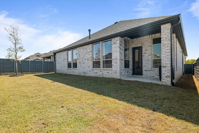 back of house with brick siding, a shingled roof, a lawn, a fenced backyard, and a patio