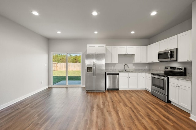 kitchen featuring sink, light stone counters, wood-type flooring, white cabinets, and appliances with stainless steel finishes