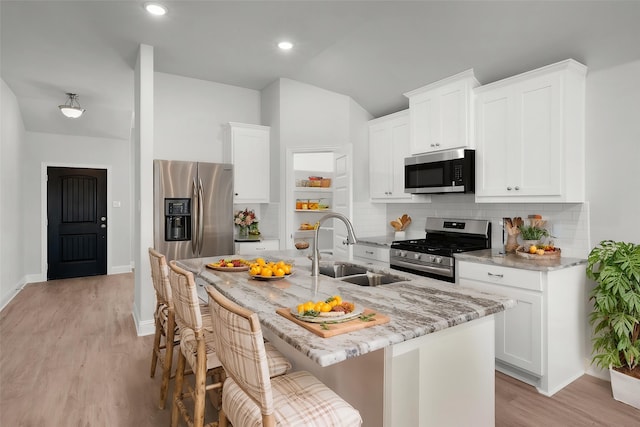 kitchen with lofted ceiling, light stone countertops, a sink, tasteful backsplash, and appliances with stainless steel finishes